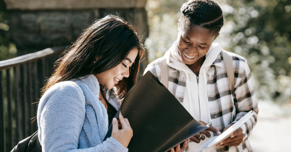 Duas jovens estudantes olhando documentos ao ar livre, simbolizando o acesso a diferentes opções de financiamento estudantil na Tuiuti.